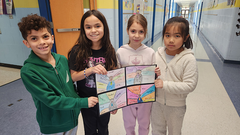Four second grade students hold drawings of Martin Luther King Jr. and the words that describe him.