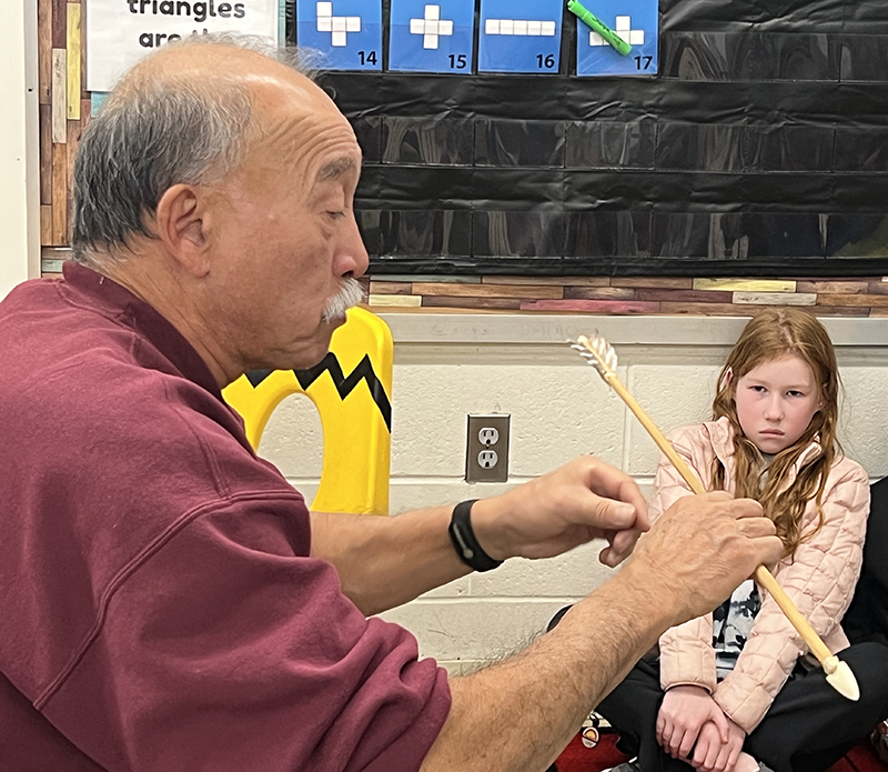 A man wearing a red shirt holds out a handmade arrow.