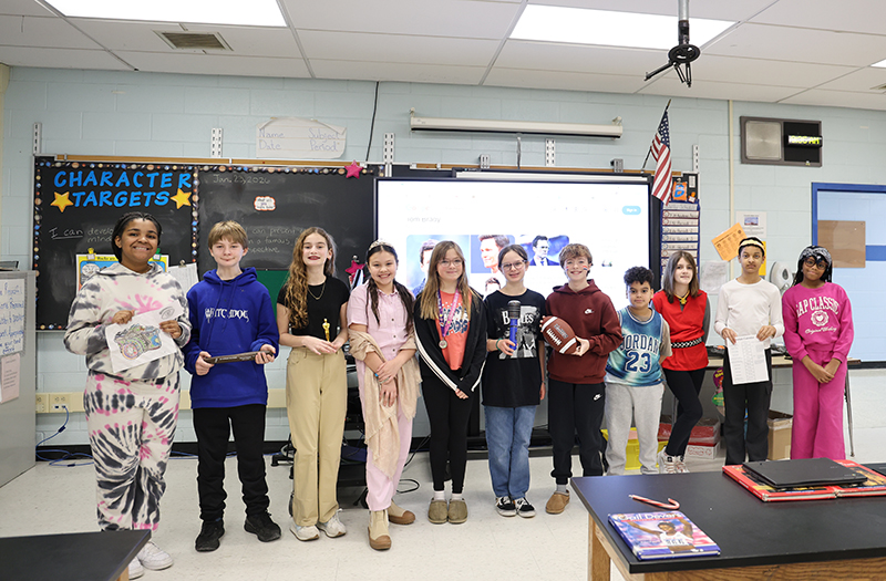 A group of 11 middle school students stand wearing items representing certain people.