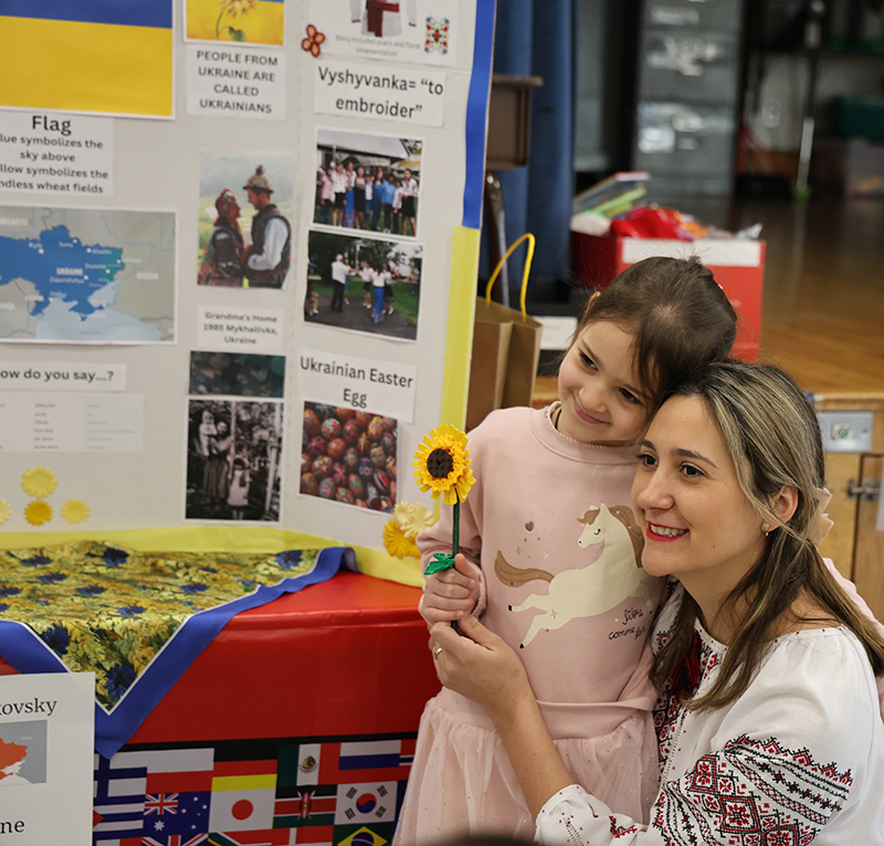 A woman squats down with a little child and holds a sunflower.