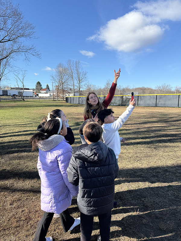 Several elementary students and a teacher hold up little devices to measure the wind speed.