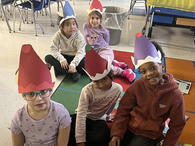 A group of five second-grade students with paper elf hats on their heads.