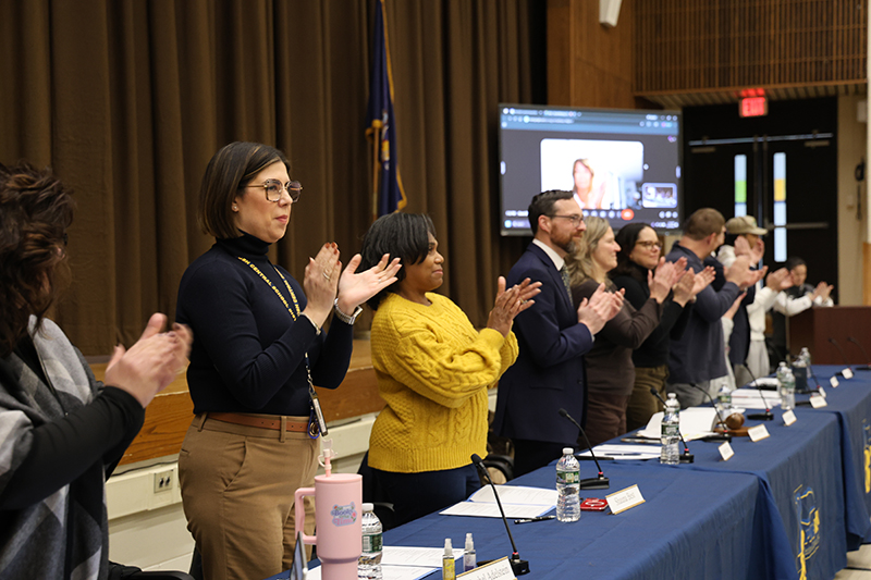 A line of adults stand and clap.