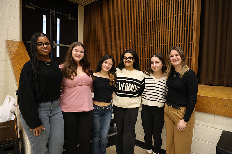 A group of six women stand together, arm in arm.
