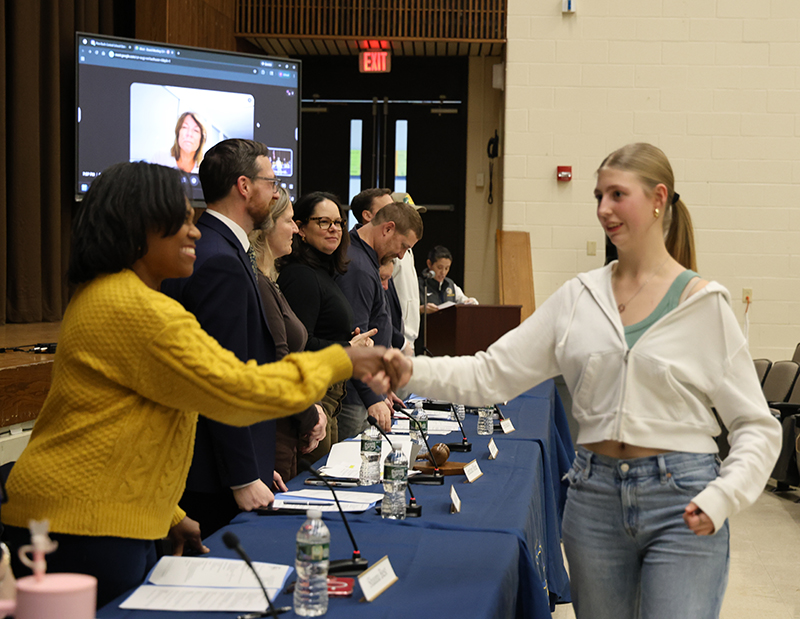 A young woman with long blonde hair shakes hands with a woman who is standing in a line with other men and women.