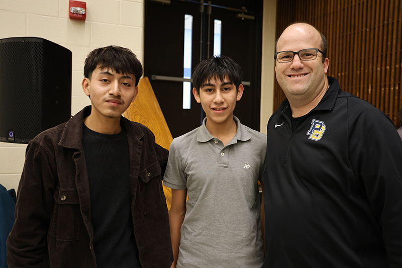 a MAN STANDS WITH TWO YOUNG MEN.