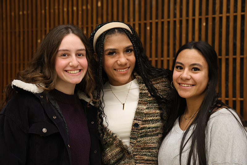 Three young women stand together and smile.