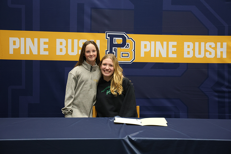 A girl with long blonde hair smiles and hugs a younger girl, who is also smiling.