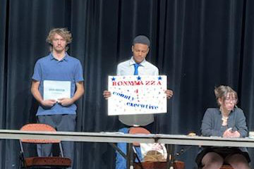 High School students on a stage hold campaign signs.