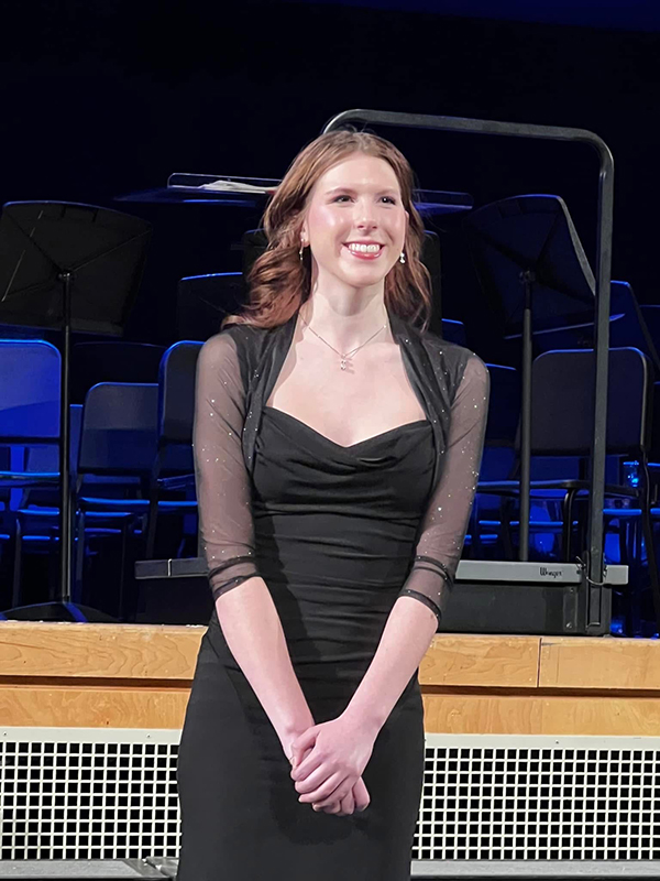 A high school girl with shoulder length light hair wearing a black dress smiles broadly.