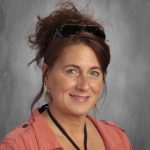 A woman with her hair pulled up smiles. she is wearing a peach colored shirt.