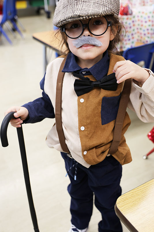 A young kid dresses with a cap, bow tie and holds a cane to look like an old man.