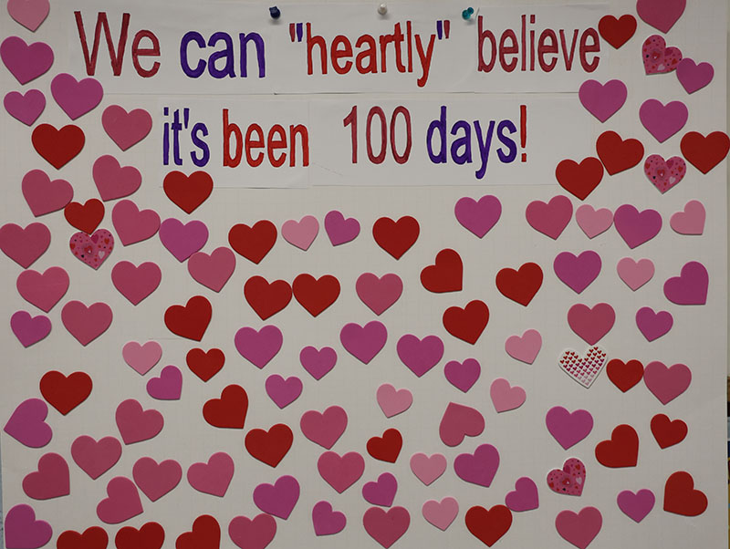 A large poster says We can heartly believe it's been 100 days! There are all red and pink hearts all around it.