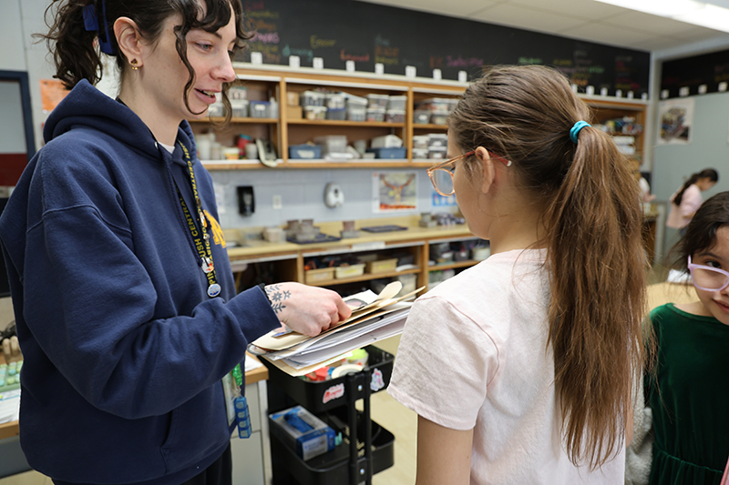 A woman with long dark hair helps a student.