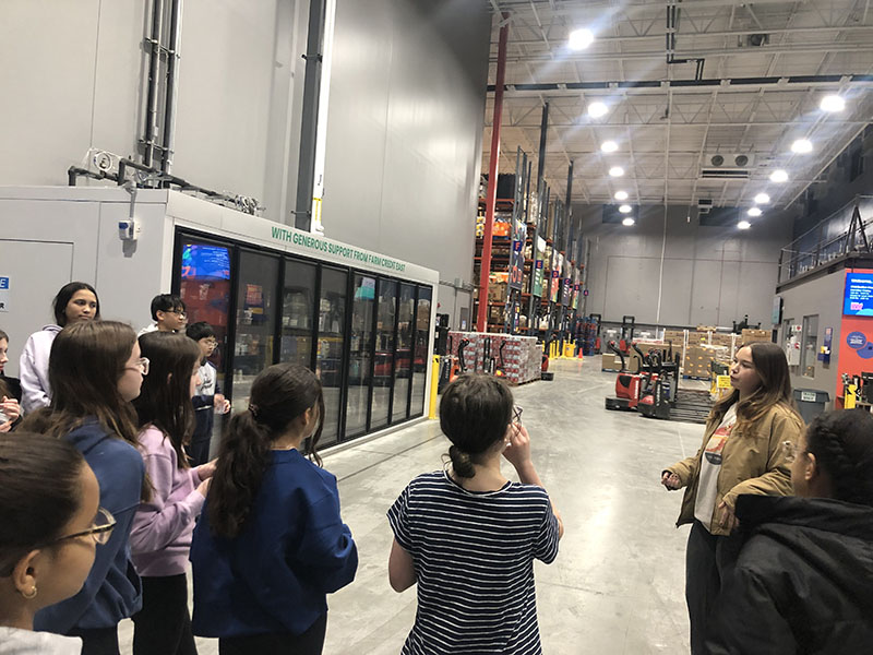 A large warehouse with a big freezer on the left. A group of middle school students stand in a group.