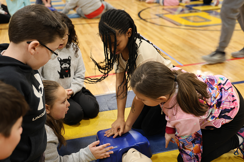 A fourth-grade girl performs CPR on a manikin as her classmates watch.