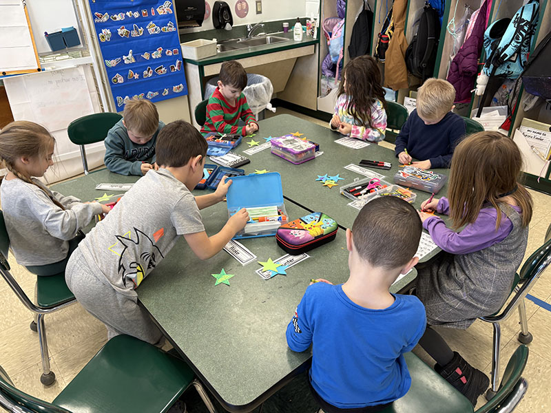 A group of kindergarten kids sit around a table making magic wands.