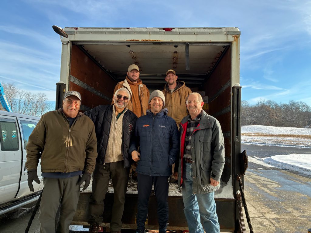 A group of six men by the opening of a box truck. They are smiling.