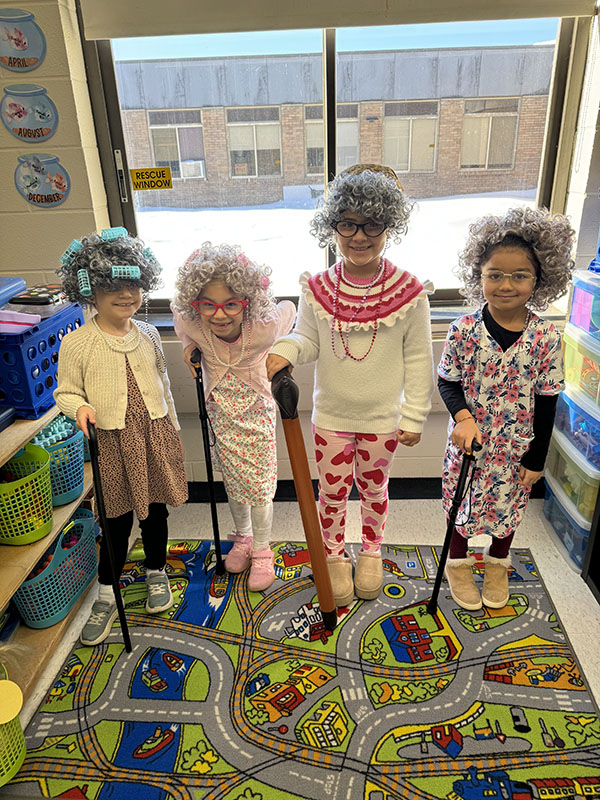 Four young elementary age girls dressed like old ladies, with gray wigs, curlers and canes.