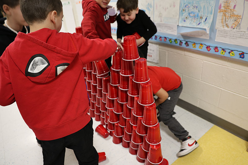 Younger elementary boys stack large red cups.