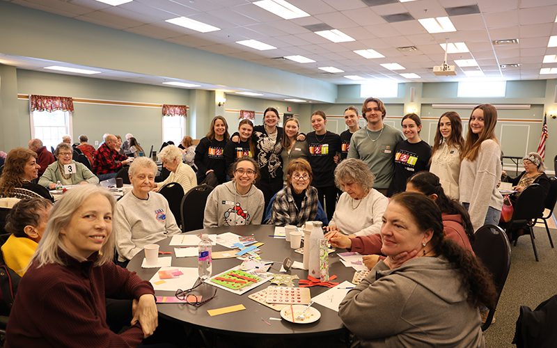 PBHS NAHS whole group web A group of 10 high school kids gather around a round table with senior citizens sitting at it. Everyone is smiling.