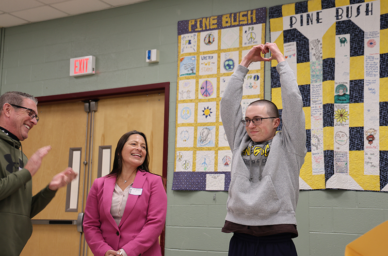 A young man smiles as he puts his hands over his head in the shape of a heart.