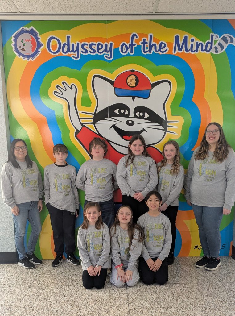 A group of 7 elementary students and two adult women stand in front of a very colorful wall that says Odyssey of the Mind.