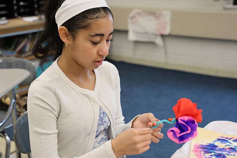 A girl sits and makes flowers of paper.