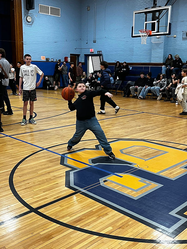 A middle school boy gets ready to heave a basketball from half court. He is reaching way back to throw it.