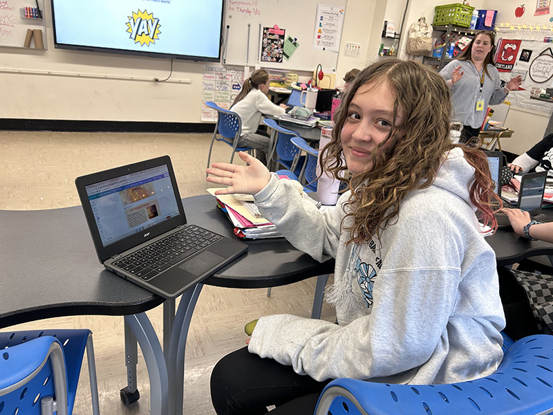 A middle school girl smiles and shows a website she created on her Chromebook.