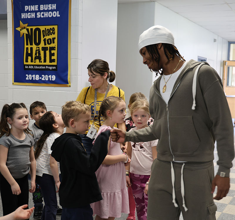 A high school student gives a fist bump to a kindergarten student while others are standing around.