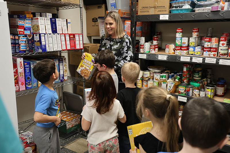 A line of kindergarten students stand waiting to put their box of cereal on a shelf.