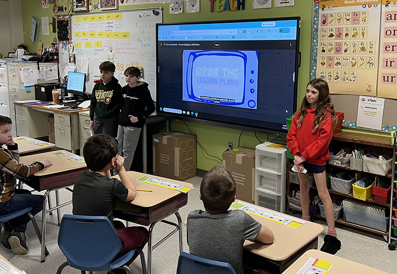 Three fifth-graders stand in front of a classroom talking to younger kids about bullying and being an upstander.