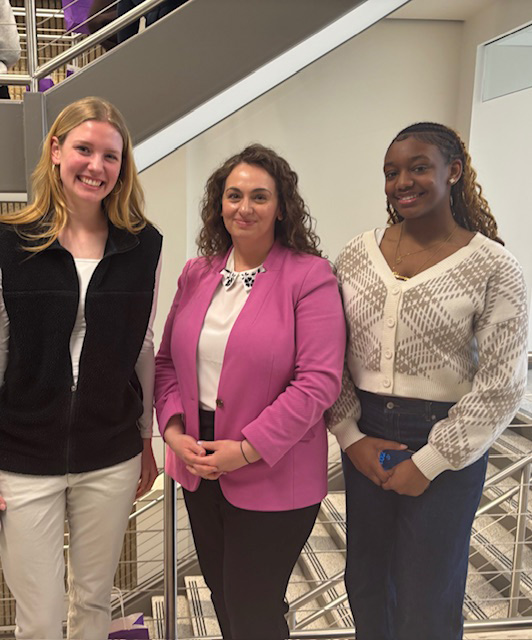 Two high school young women stand with a woman at a conference.