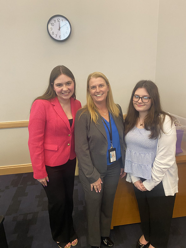 Two young women stand with a woman at a conference.