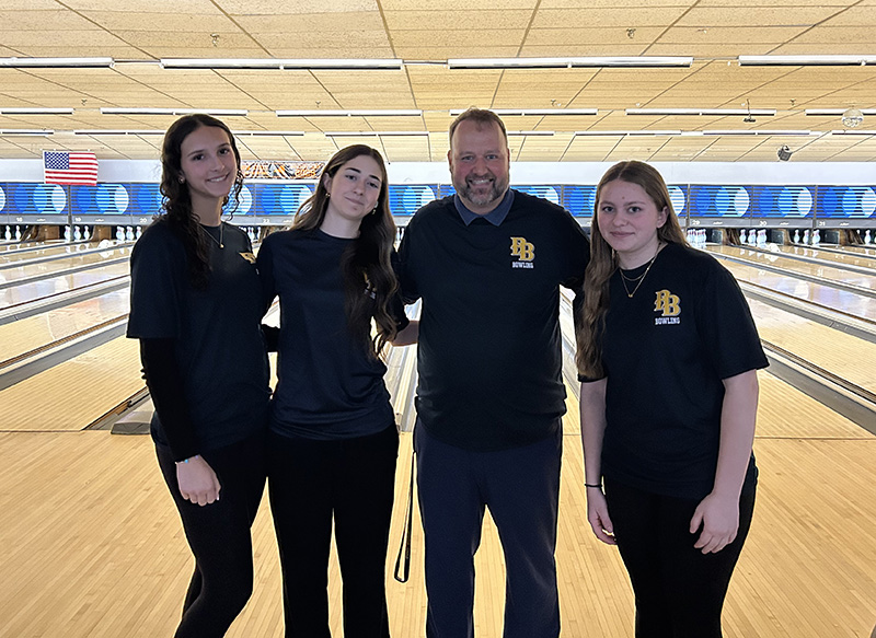 Three young women stand with a man at a bowling lane.