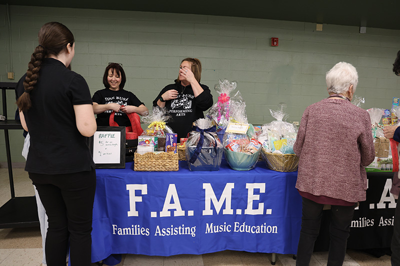 A table with FAME on the front and a bunch of baskets to be raffled on it.
