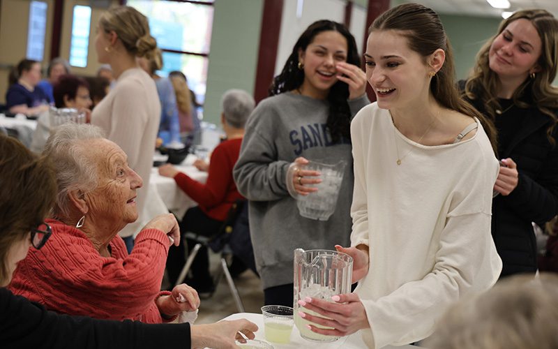 A high school girl pours water into someone's cup.