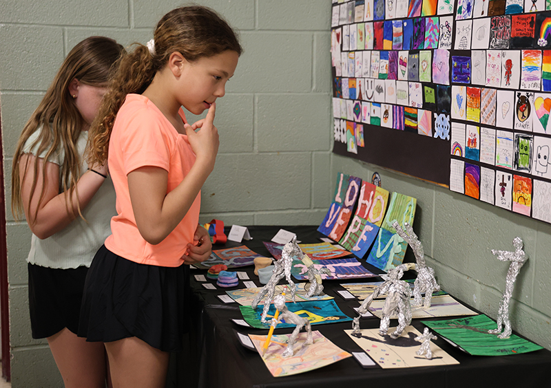 Two girls look at 3d art on a table 