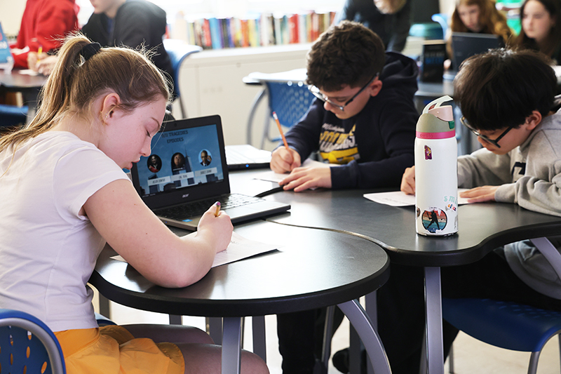 A group of four middle school kids write as they listen to a podcast.