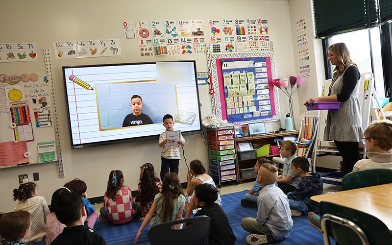 A woman holds a large globe showing a class of children