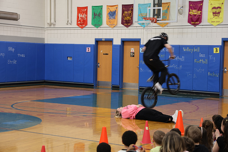A man riding a bike jumps over a person lying on the floor.