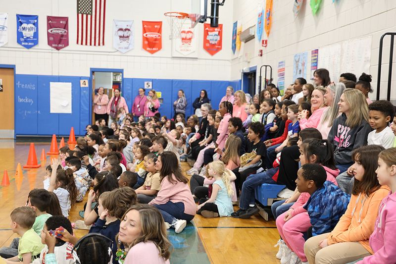 A large group of kids watch as a man rides his BMX bike.