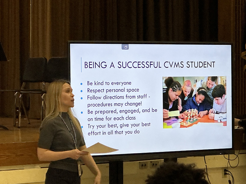 A woman stands beside a screen that tells how to be a successful CVMS student.