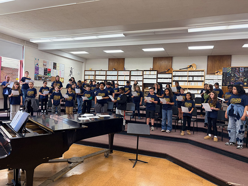 A large group of elementary students standing on risers singing.