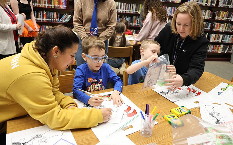 Two kindergarten kids are coloring Dr. Seuss characters, with high school kids helping them.