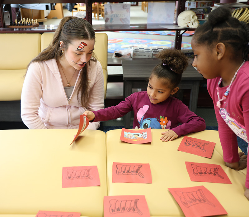 Two kindergarten kids play a matching game with a high school girl helping them.