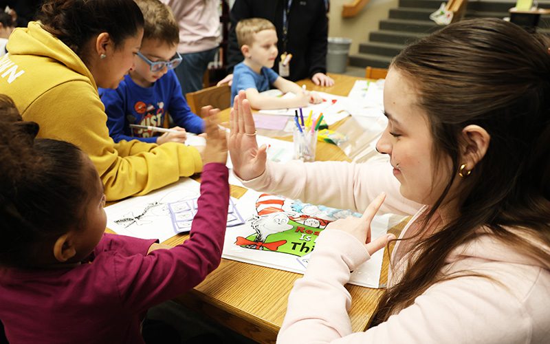 A high school girl gives a high five to a kindergarten kid.