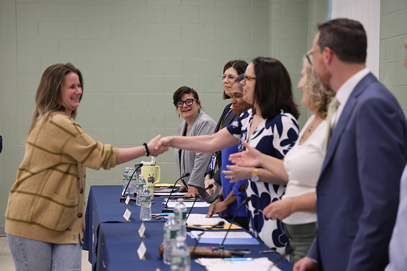 A woman shakes hands with another woman, while others stand by ready to shake her hand also.