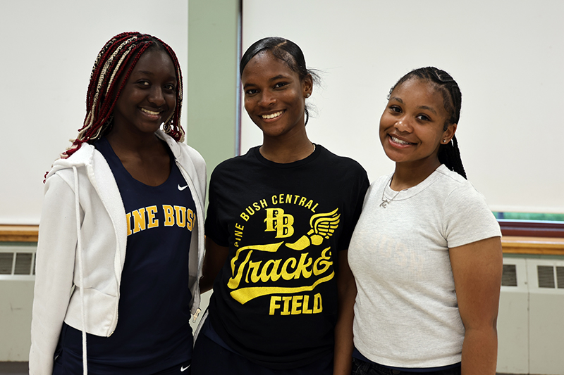 Three young women smile and stand together. Two have Pine Bush track and field shirts on.